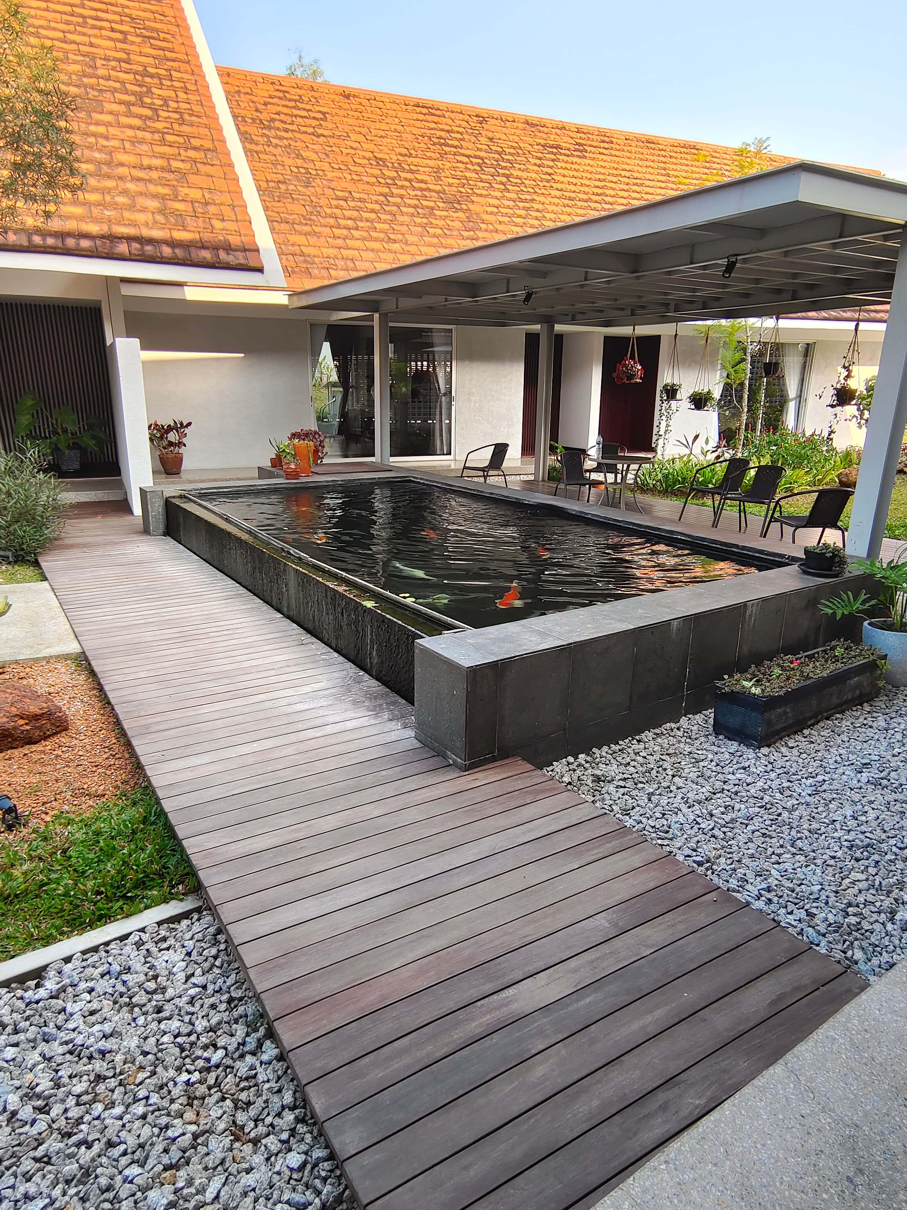 Outdoor hardwood deck walkway bordering koi pond at Kowi Bangka residence by Reywood Indonesia
